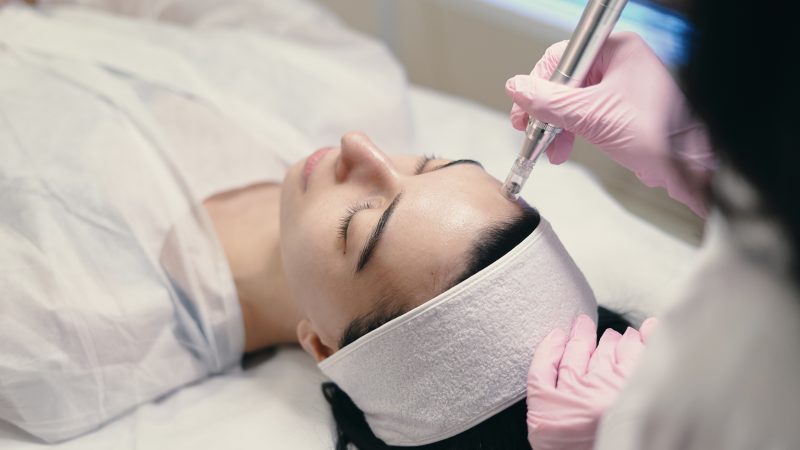 Model with closed eyes and hand's of doctor. Rejuvenating facial treatment. Model getting lifting therapy massage in a beauty SPA salon. Cosmetological clinic, procedure.